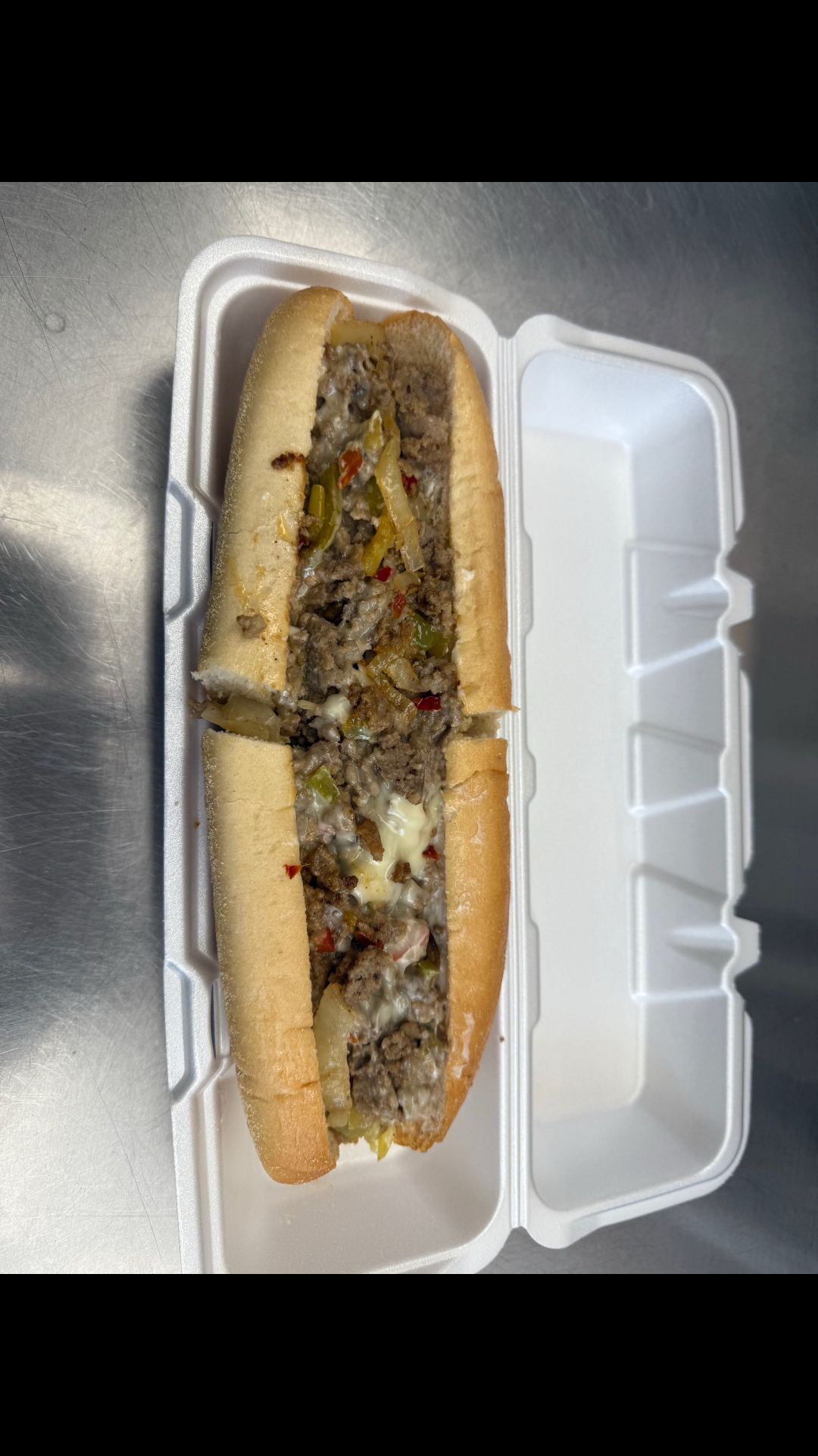 Philly cheesesteak on a hoagie roll with peppers, onions and melted cheese in a takeout container